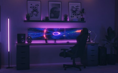 Modernes Gaming-Setup aus drei Monitoren auf einem Schreibtisch mit violetter Ambiente-Beleuchtung