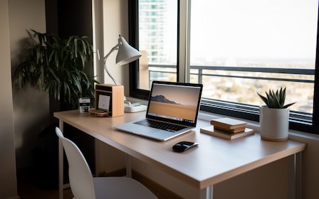 Laptop steht auf Schreibtisch vor Fenster Ein Laptop steht auf einem Schreibtisch vor einem Fenster, geben von PFlanzen mit Blick ins Freie.