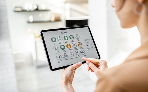 Die Zukunft zu Hause Eine Frau hält ein Tablet in der Hand. Auf dem Tablet sind mehrere Apps mit Smartphone-Technologie abgebildet, die das Licht und die Energie zu Hause steuern.